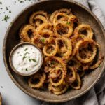 Golden crispy onions made in the air fryer, served in a rustic bowl with fresh herbs.