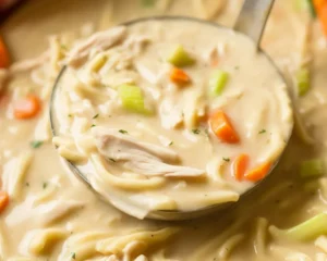 Bowl of creamy chicken soup with vegetables and herbs for a comforting meal.