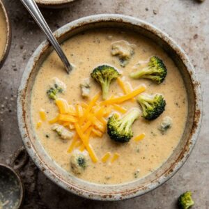 Creamy broccoli cheddar soup with melted cheese in a rustic bowl.