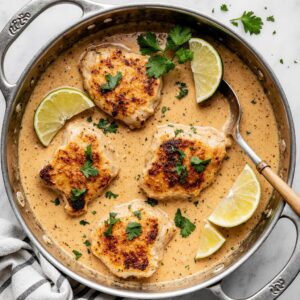 Golden seared chicken thighs cooking in creamy coconut lime sauce with fresh cilantro.
