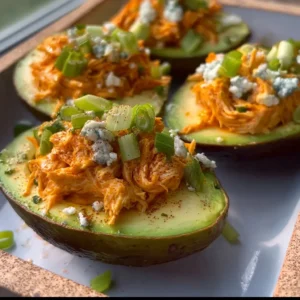 Buffalo Chicken Stuffed Avocados served on a plate with fresh herbs.