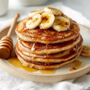 Fluffy banana bread pancakes stacked and topped with syrup and banana slices